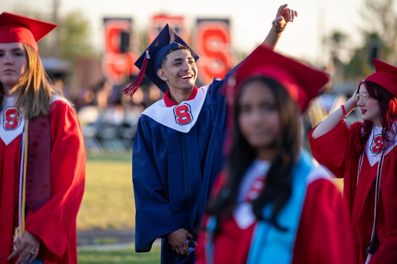 A Sahuaro grad smiles and waves to a friend in the crowd of fellow graduates