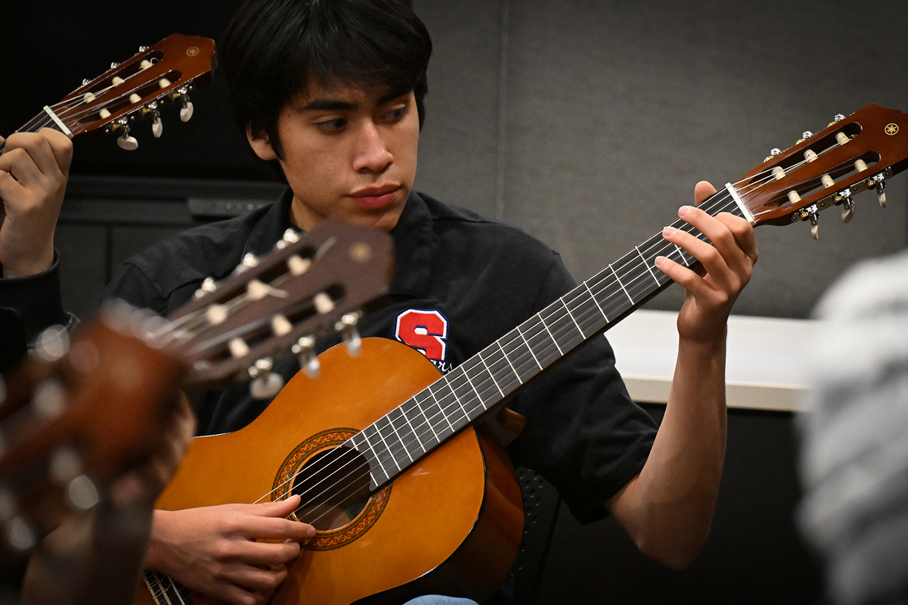 A teen boy with dark hair plays his guitar