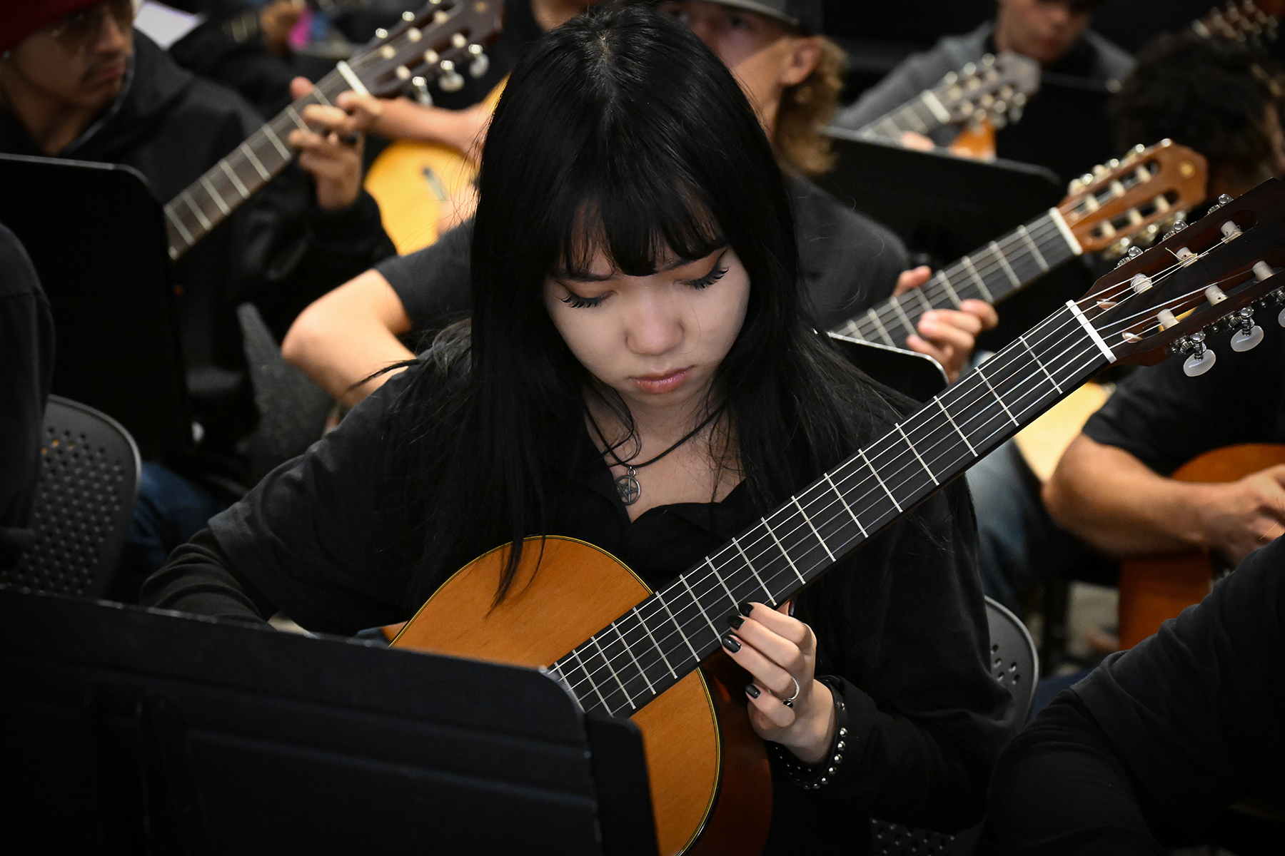 A teen girl with dark hair looks down at her guitar as she plays