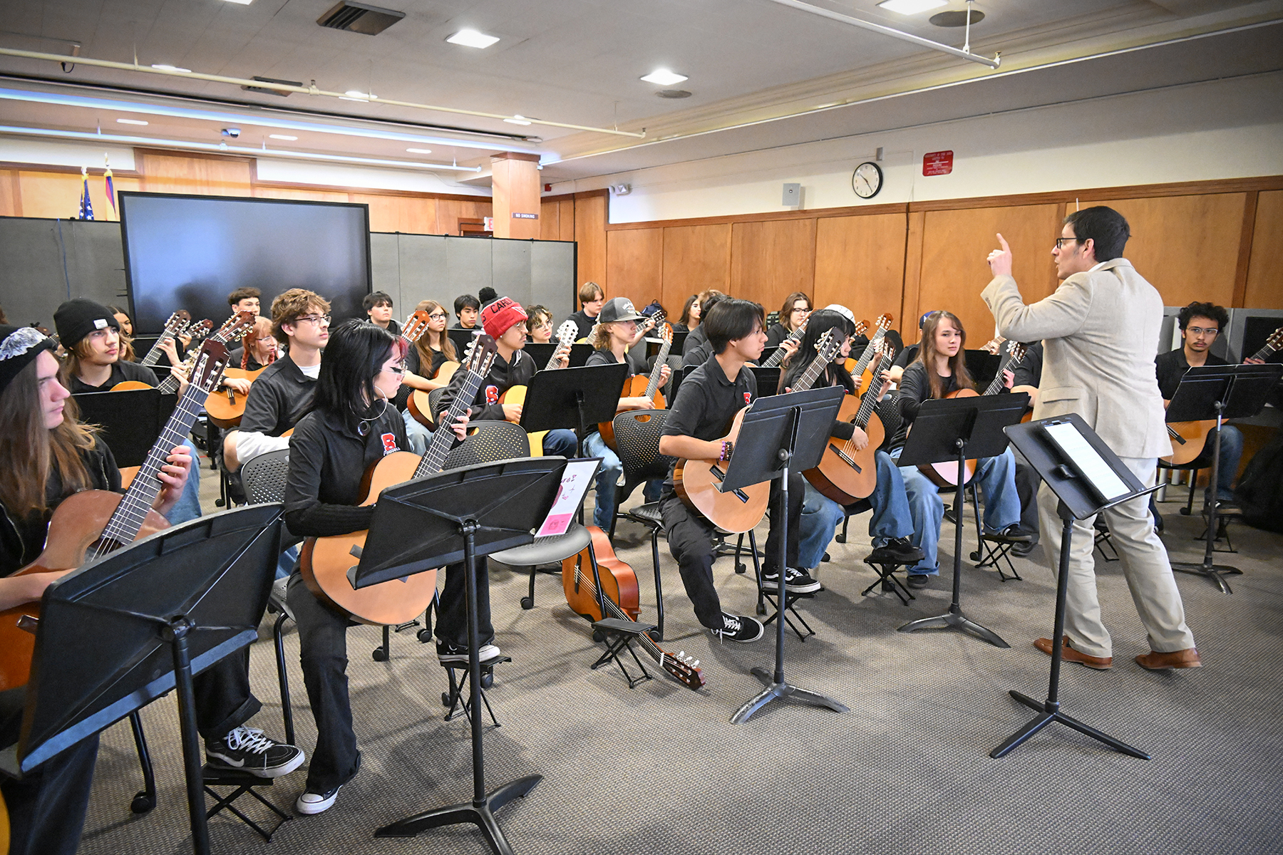 A music teacher directs the advanced guitar orchestra