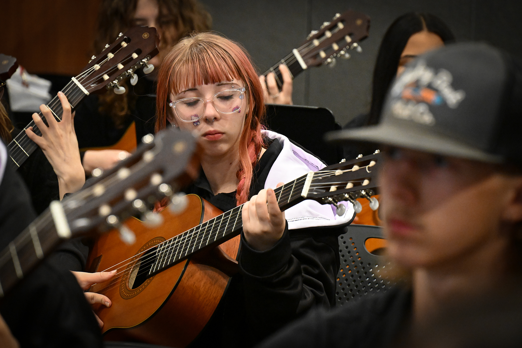 A teen girl with glasses and stickers on her face plays her guitar