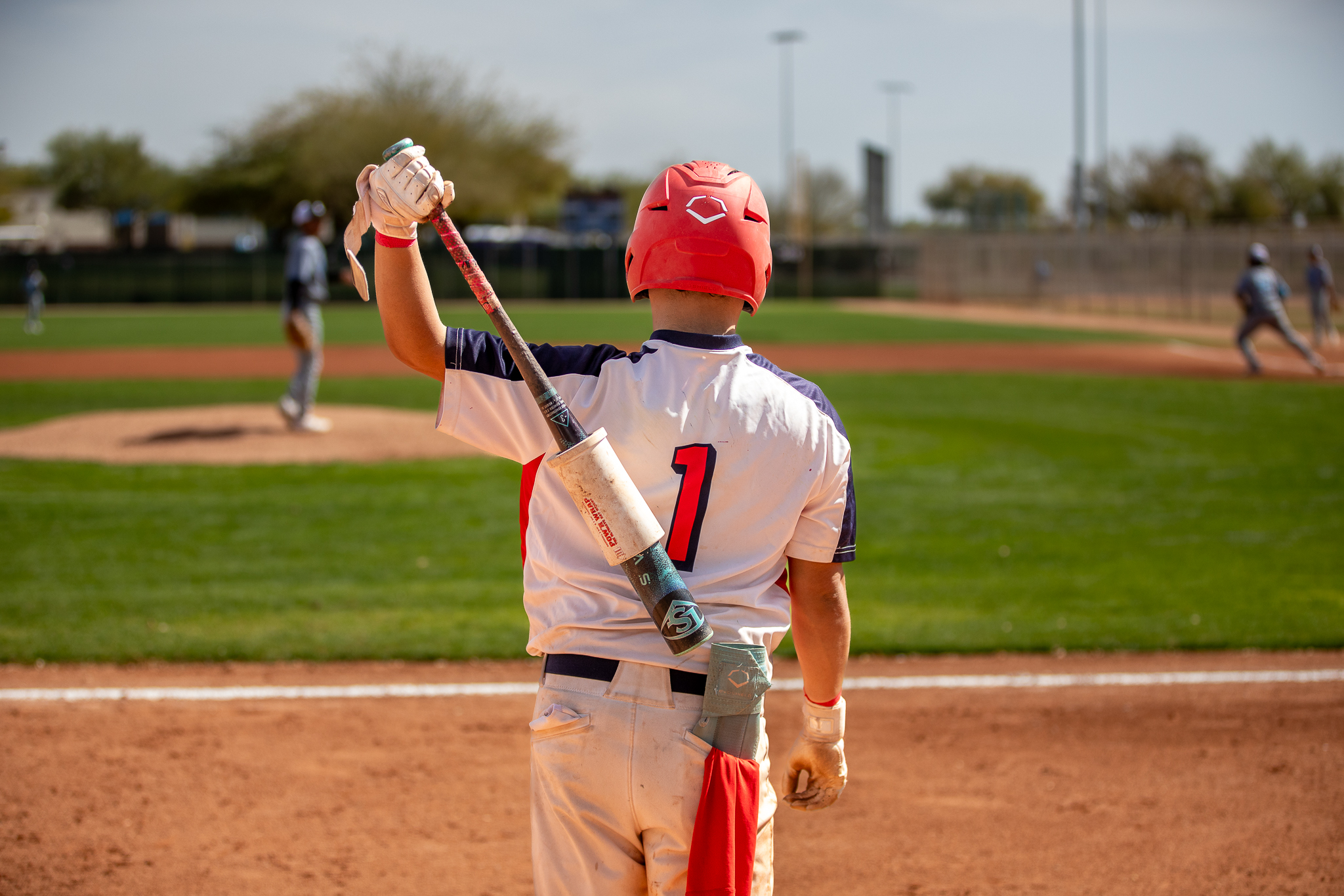 A baseball player in a number 1 jersey holds the bat behind his back as he looks out onto the field