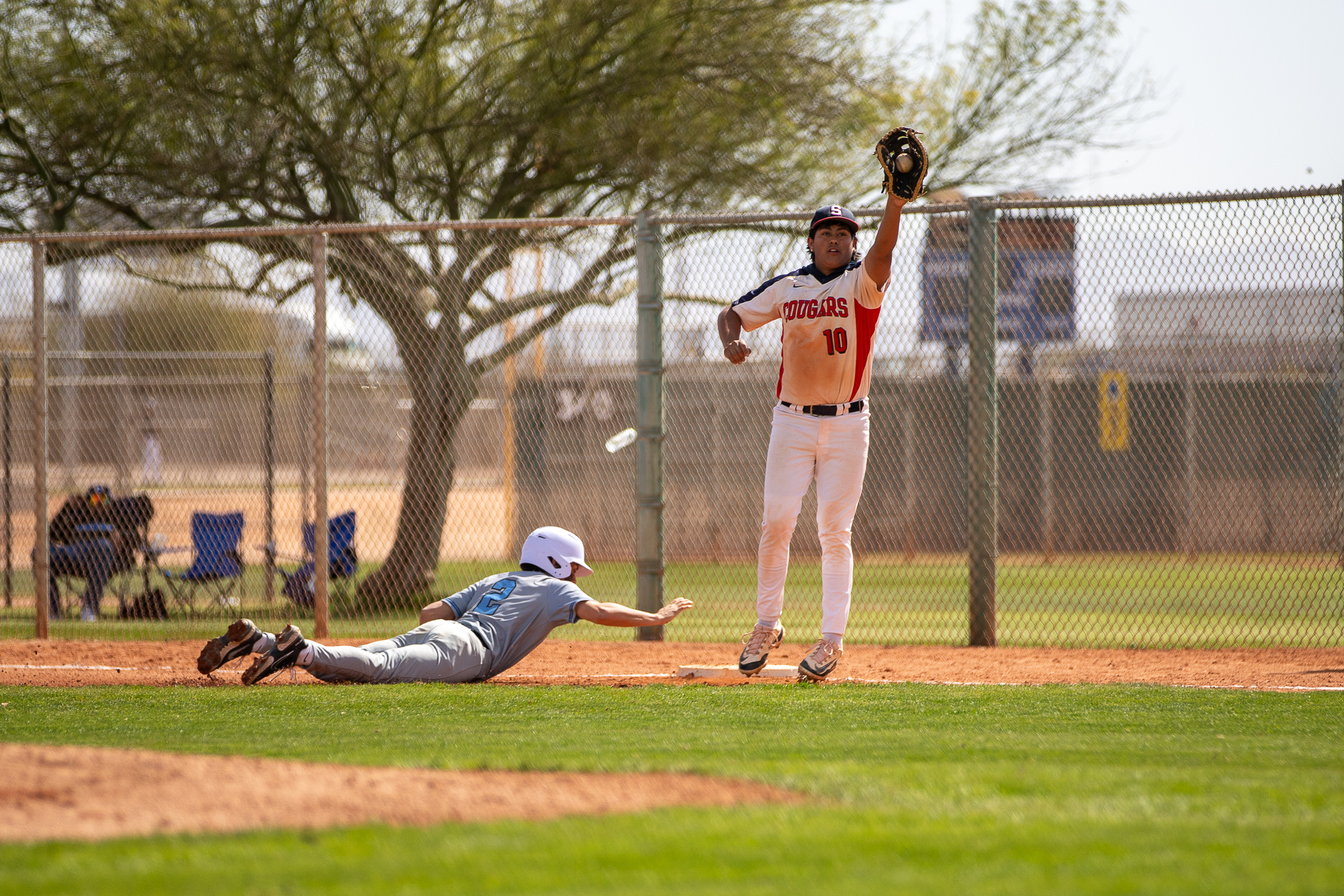 A Sahuaro player jumps up to catch the ball in his mitt as an opposing player slides into the base