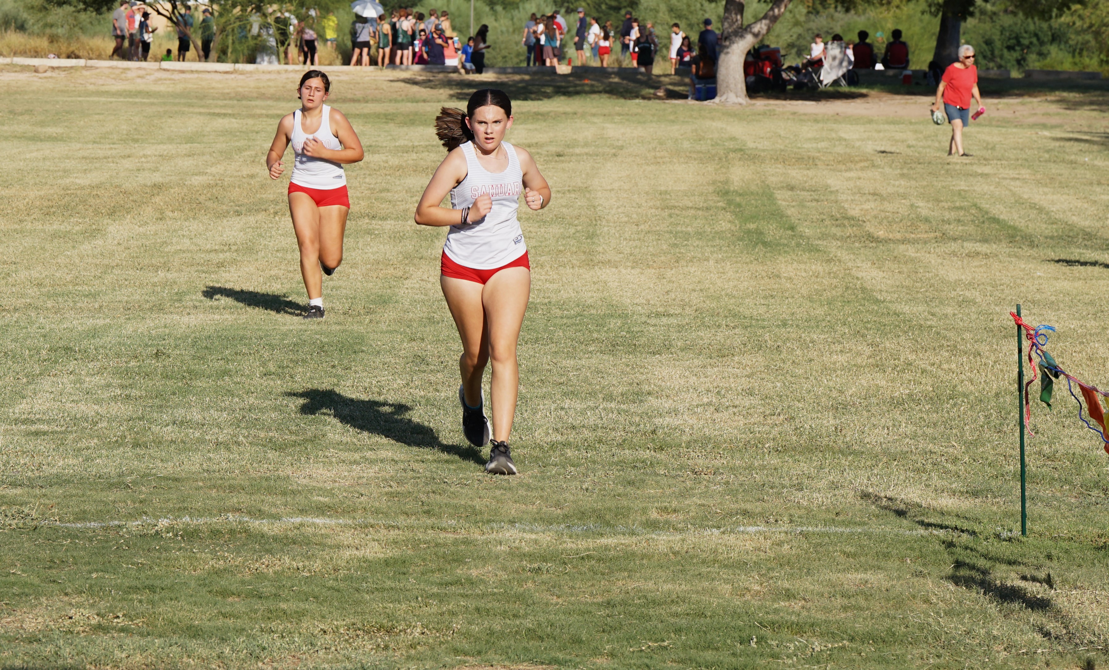 Two Sahuaro cross country athletes run across the grassy field