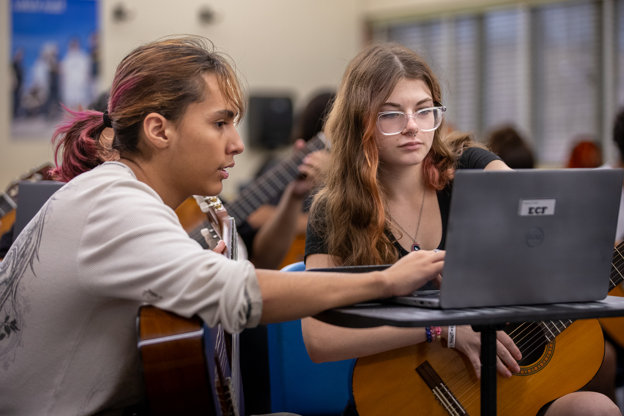 Two girls hold their guitars and look at their laptop