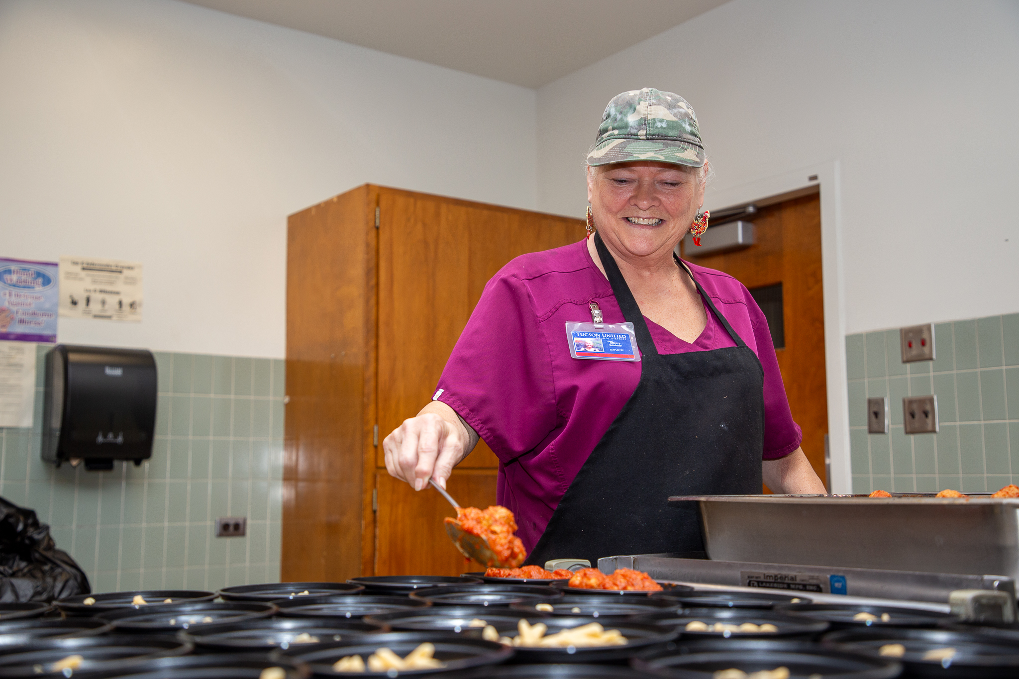 A woman smiles as she serves food in the cafeteria