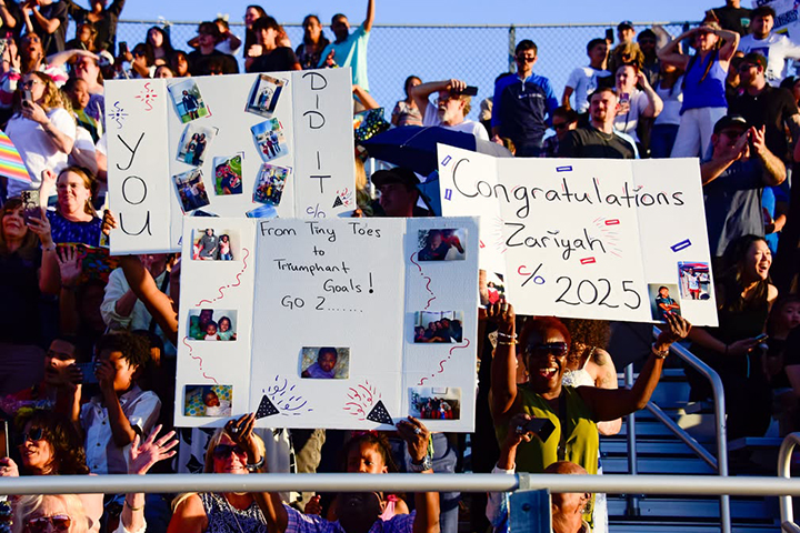 Families hold up posters to cheer on grads from the bleachers