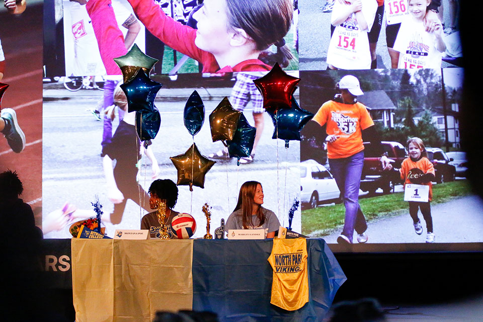 Two student athletes look up at the slideshow of photos of their accomplishments through the years