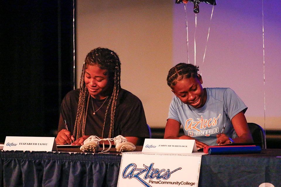 Two girls sign their letters of intent