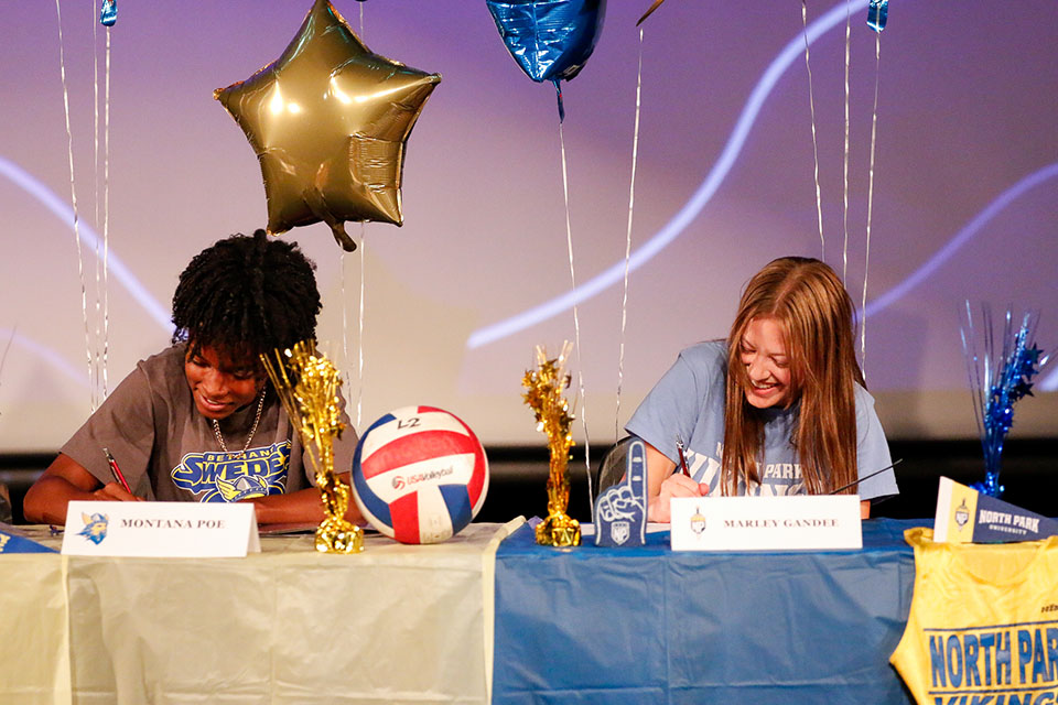 Two teen girls smile as they sign their letters of intent