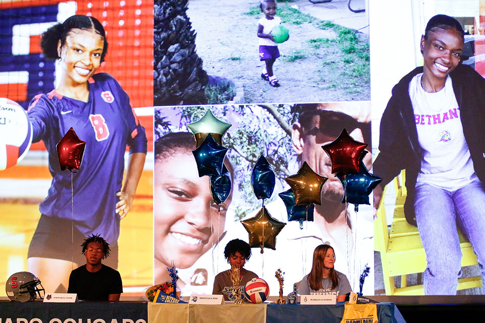 Three student athletes sit at a table below a screen showing their athletic highlights