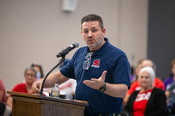 A man in a blue polo talks into a microphone