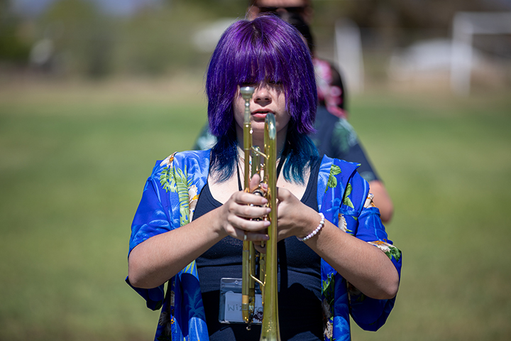 A girl with purple hair holds her trumpet in front of her