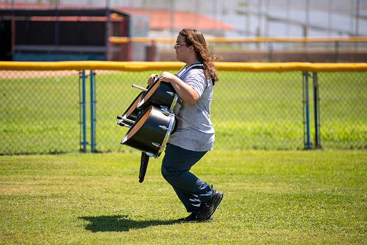 A girl marches across the field holding a drum set