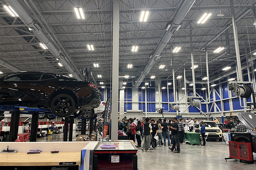 A sedan on a lift with a group of students chatting in the background