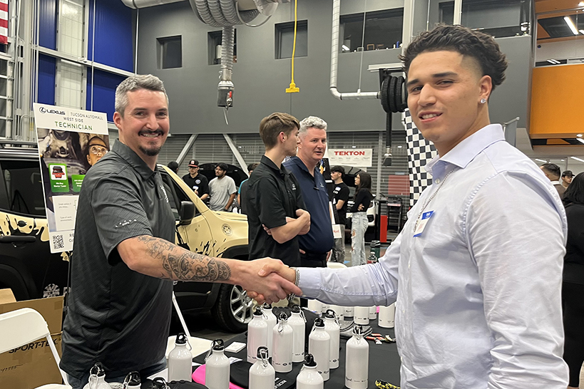 A teen boy and man shake hands and smile