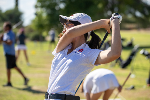 A teen girl swings her golf club over her shoulder