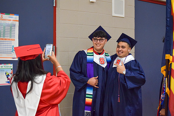 A graduate in a red cap and gown takes photos of two grads in blue caps and gowns