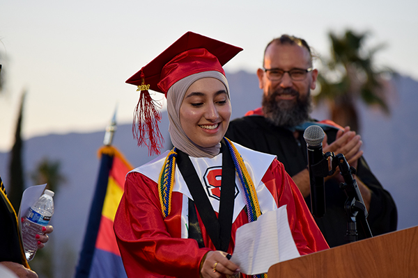 A teen girl in a red cap and gown gets ready to speak during the graduation ceremony