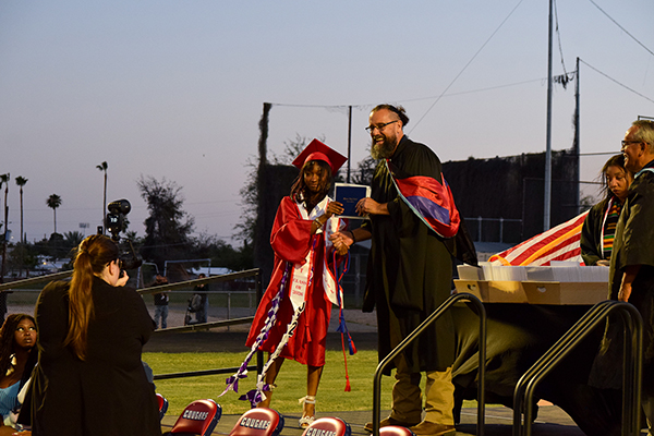 A teen girl accepts her diploma from the principal