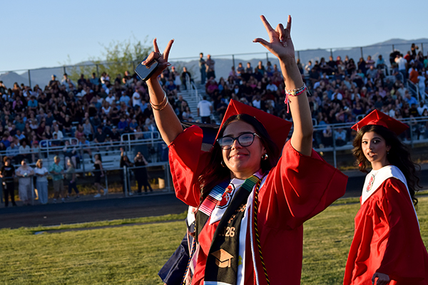 A teen girl throws up hand signs as she walks across the field during graduation