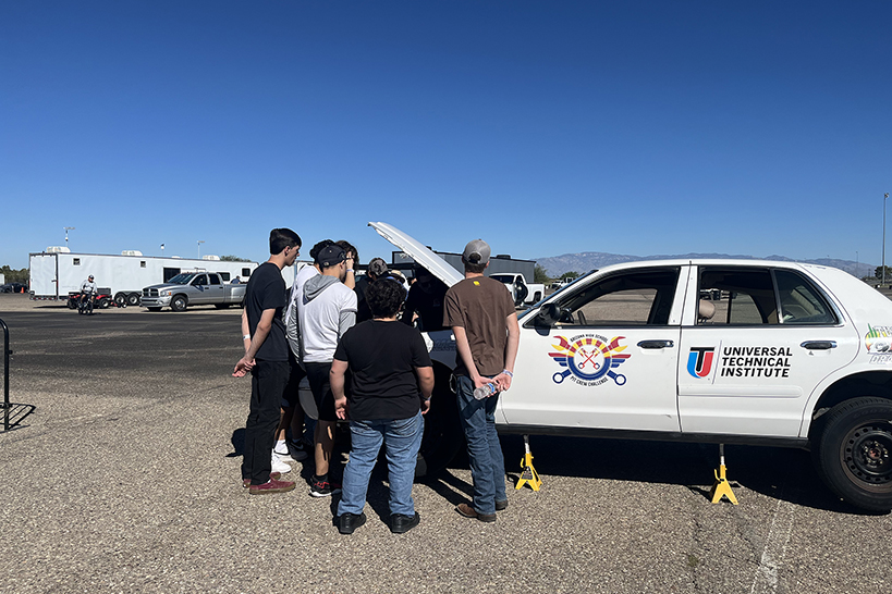 A group of teen boys gather around a white vehicle outside
