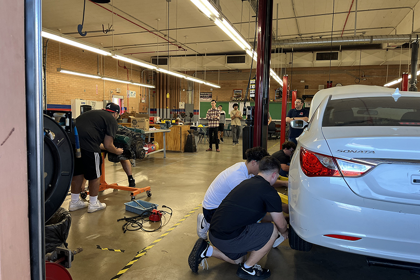 Teen boys crouch down working on a white car