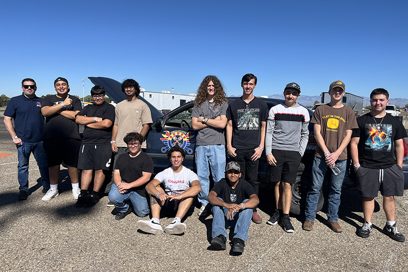 A group photo with teen boys posing in front of a black car