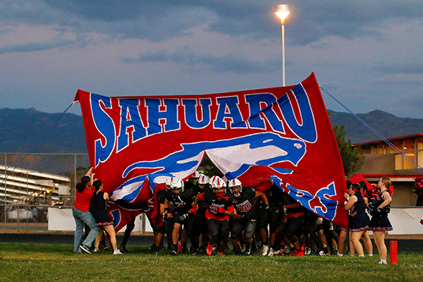 The football team runs through the Sahuaro banner
