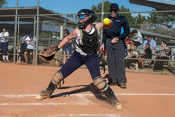 The catcher swings her arm to throw the softball