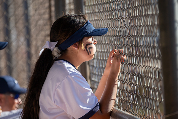 A girl watches her teammates from the dugout