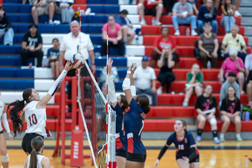 A teen girl jumps up to hit the volleyball back over the net