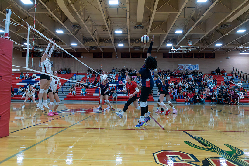 A teen girl jumps up to spike the volleyball