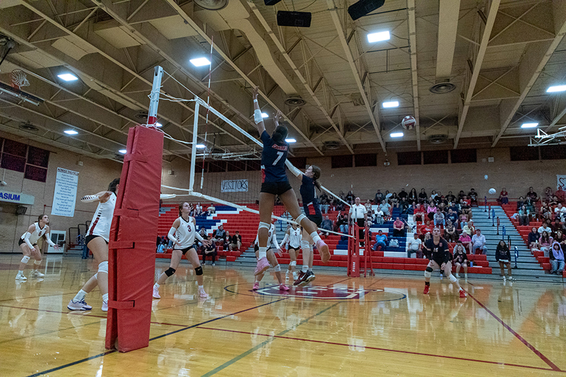 Two teen girls leap up to hit the volleyball back over the net